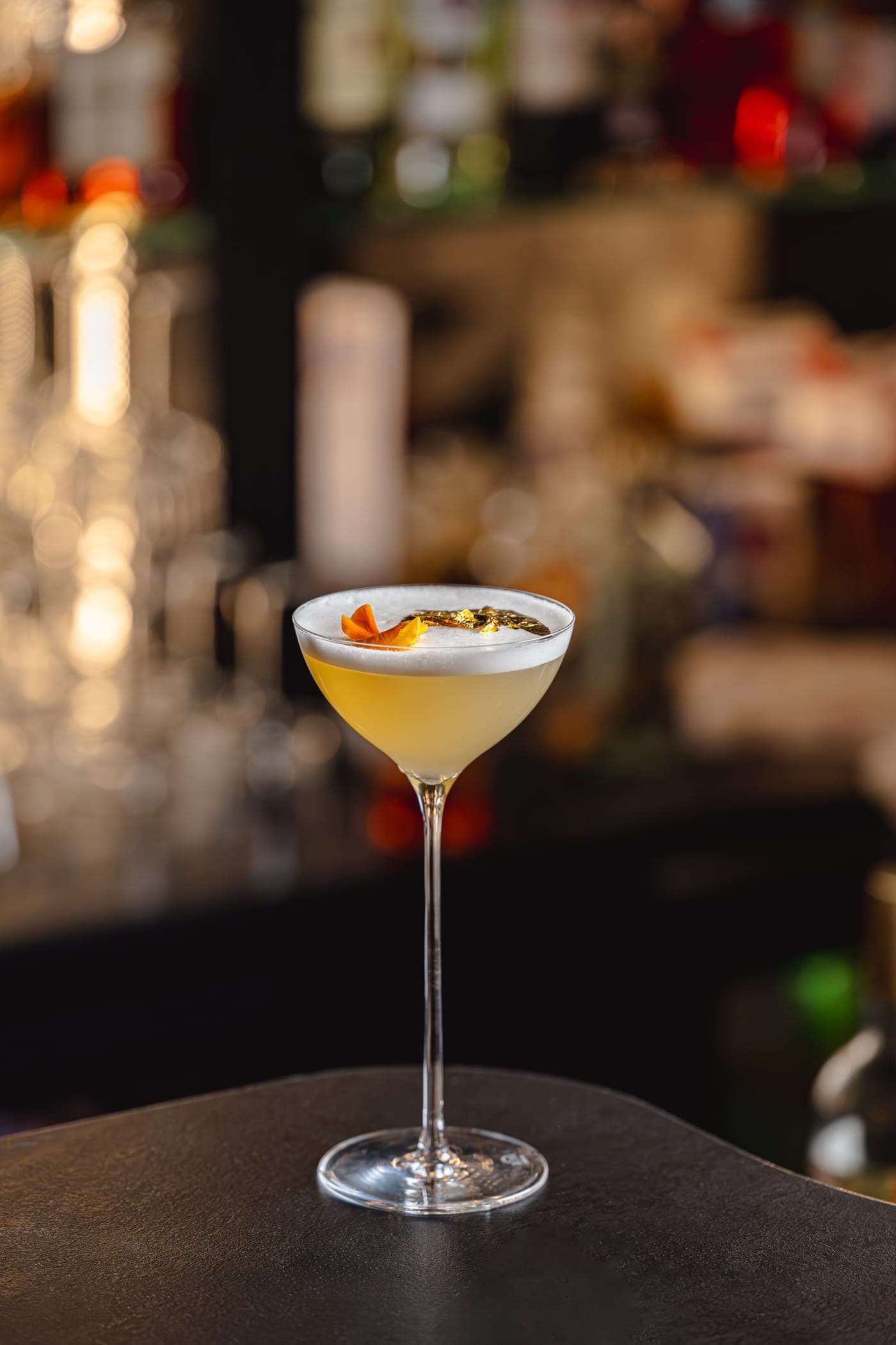 Zeița Carpaților — cocktail auriu cu spumă fină și sclipiri de foiță de aur, servit într-un pahar coupe la bar